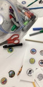 Photo of tribal seals printed out with crayons and markers available on a white table for Indigenous students at SPIRIT program.