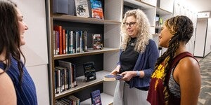 A group of three people standing and talking in front of a bookshelf