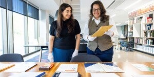 Two people standing in front of a table filled with archival materials talking with one another