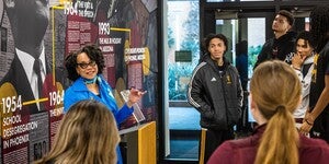 A woman speaks to students next to a historical display wall with civil rights content.