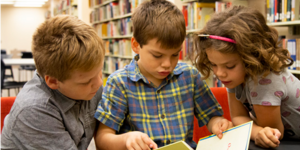 Three school-age children read a book from the Curriculum Collection together in ASU's Hayden Library. Photo by Amy Carolyn Watson, ASU Library.