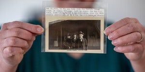 A person holding a vintage black-and-white photograph in a clear sleeve with a typed note above it.