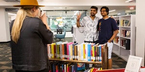 Person taking a photo of two students standing in front of a cart filled with books