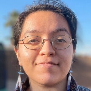 Headshot of Elena Dominguez smiling at camera wearing beaded earrings and glasses