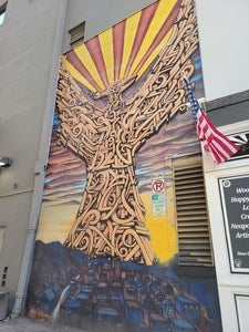 Photo of fist mural Breeze showed the Labriola Center. The Phoenix is made up of golden/copper spirals and rises from the city, which is covered in a blue hue from the rising and setting sun. "South Mountain" is to the left with the electrical towers standing erect, with their lights atop, barely brushing the sky..