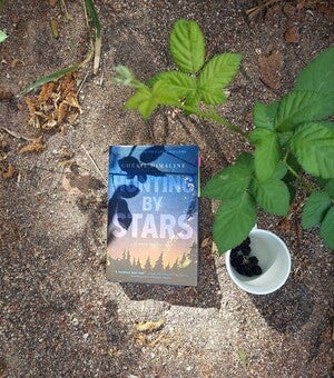 Photo of Hunting by Stars book on the ground with a cup of wild Blackberries.