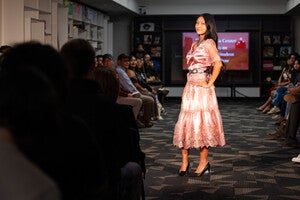 Model in a pink dress on a runway surrounded by an audience.