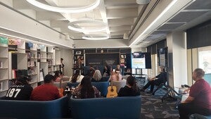 Director Alex Soto (Tohono O'odham) speaking in front of audience with Delbert Anderson (Diné), Julia Keefe (Nez Perce), and Jacob Moore (Tohono O'odham) seated.