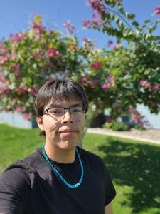 Photo of Colton Jim (Diné) wearing a black t-shirt and turquoise necklace