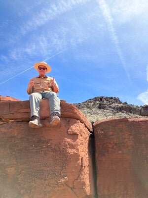 Photo of Eli Shepherd (Dine') sitting on large red rocks