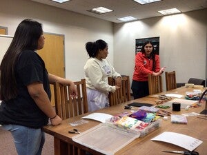 Three women standing at a table with art materials having a discussion