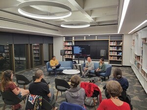 Audience members sittings in chairs with a group of individuals sitting on chairs having a panel discussion.