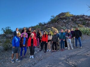 A group of people wearing winter clothing posing outside near cactus and mountain terrain for a photo. 