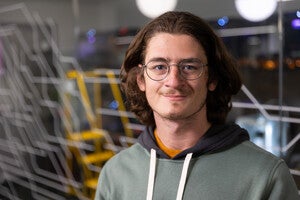 Person standing in front of Hayden Library's Makerspace 3D printers smiling for the camera