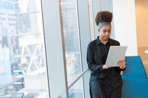 stock image of a female standing next to a window looking at a tablet computer