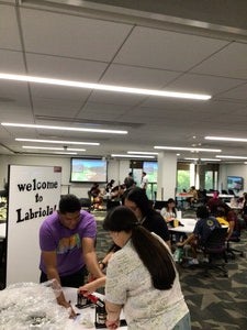 Pictured is Kevin Brown (Diné) helping Indigenous students make buttons. A "Welcome to Labriola" sign designed by Arianna Halona (Diné) is behind Kevin.