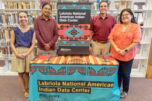 Employees stand behind a welcome table draped with Labriola National American Indian Data Center banners.