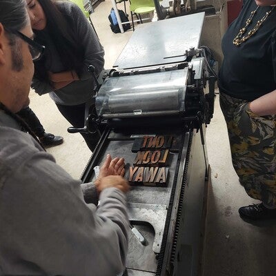 Photo of Professor Meders explaining to students the process of placement for printing letters on the printing press.