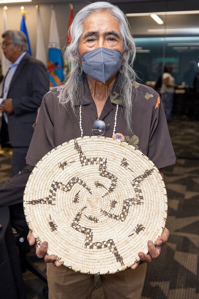 Simon Ortiz holding basket that has snake designs zigzagging from the middle outward