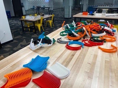 3D printed parts for face masks and shields are scattered across a table in the Hayden Library Makerspace