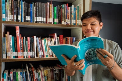 Student holding a book in from of open stacks