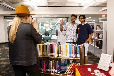 Person taking a photo of two students standing in front of a cart filled with books